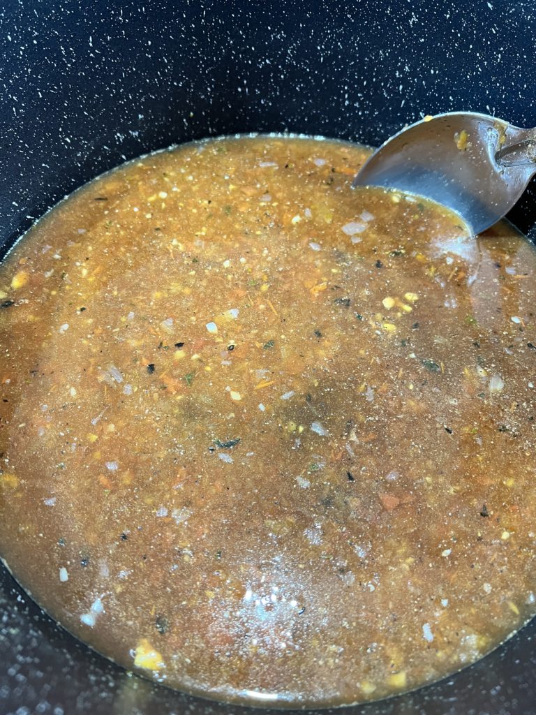 Pasta sauce, broth, minced garlic, and roux boiling in a pot