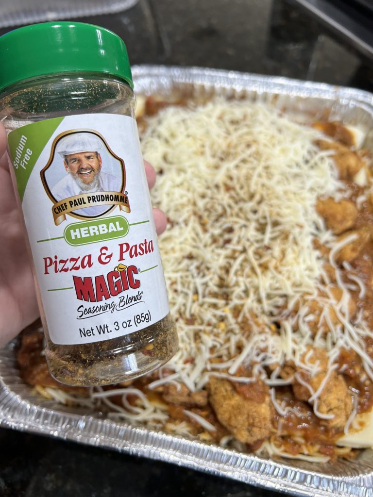 close up of pizza and pasta seasoning with a chicken parmesan in the background