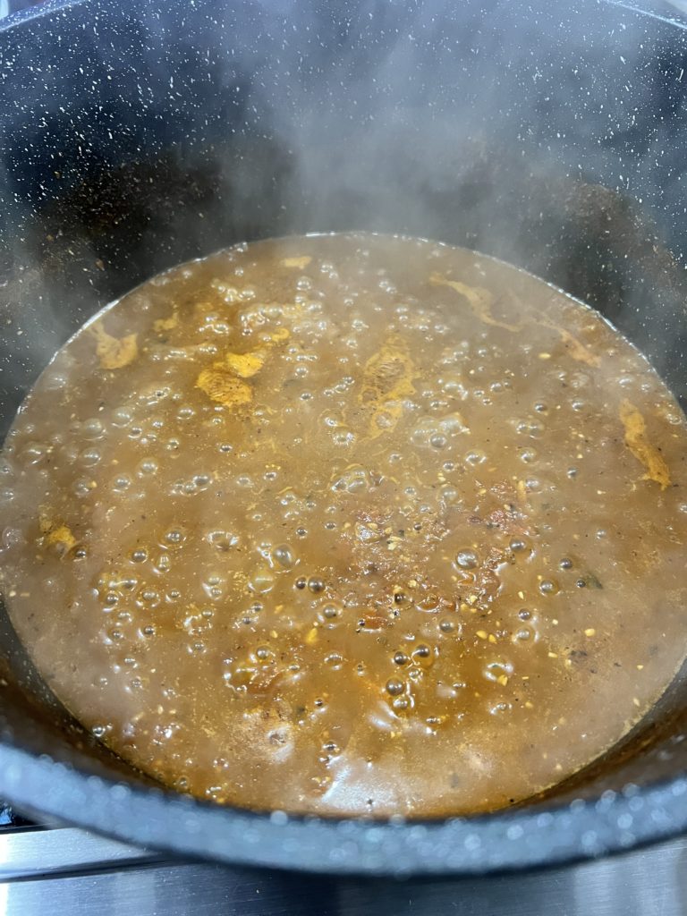 Pasta sauce, broth, minced garlic, and roux mixture thickening in a pot