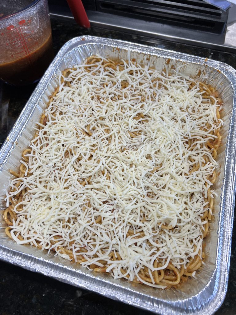 spaghetti with sauce in an baking pan topped with parmesan cheese