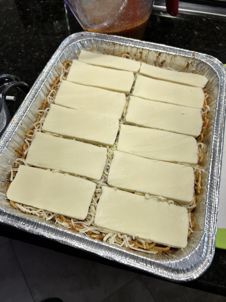 spaghetti with sauce in an baking pan topped with parmesan cheese